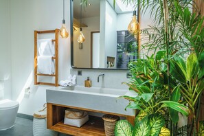 Ein modernes Badezimmer mit einem großen Spiegel, Holzregalen, einem Waschbecken und hängenden Leuchten.
