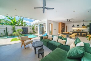 Ein modernes Wohnzimmer mit einem grünen Sofa, einem Essbereich und Blick auf den Pool.