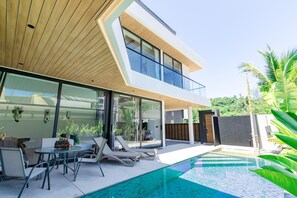 Ein modernes Haus mit Glasfassade, Swimmingpool und Sitzgelegenheit im Freien.