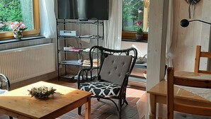 Ein gemütliches Wohnzimmer mit Fernseher, einem Holztisch, einem gemusterten Sessel und einem Bücherregal.