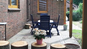 Eine Terrasse mit einer Backsteinmauer, einer Holz-Pergola, einem Tisch mit Stühlen und einem Blumentopf.