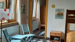 Ein Zimmer mit Schachbrettfußboden, einem fenster mit Jalousien, einem Heizkörper, einer Holztür, einem Poster an der Wand und einer kleinen Holzkabine.