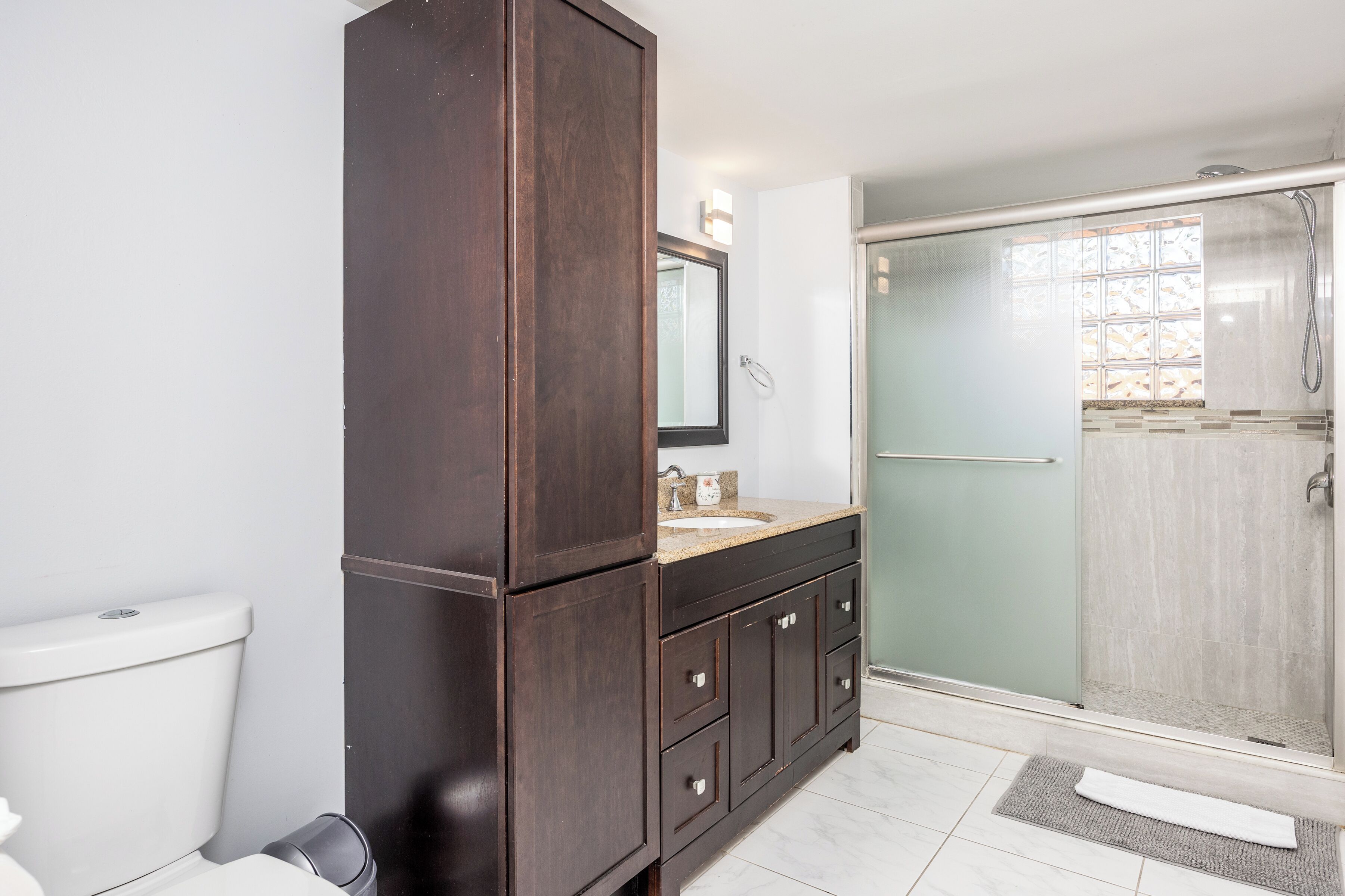 A bathroom with a dark wooden vanity, a white toilet, and a glass shower enclosure.
