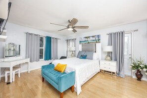 A bedroom with a bed, a desk, a chair, a blue bench, a ceiling fan, and a painting of a beach scene. - Sol Vacation:  Relaxing and Confort in one place (Largo)