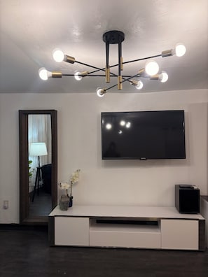 Ein modernes Wohnzimmer mit Flachbildfernseher, einer weißen Unterhaltungsanlage, einer dekorativen Vase mit Blumen und einer besonderen Deckenleuchte.