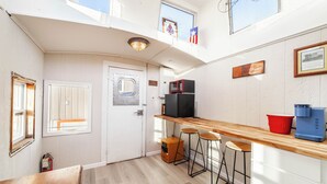 Een kleine keuken met een houten aanrecht, twee barkrukken, een koelkast en een magnetron.