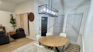 A modern living room with a round wooden dining table, white chairs, a bench, a sofa, a potted plant, a clock, and a geometric pendant light. - Remote&Travel Workers Retreat: Beautiful Rockwall home near the Harbor (Rockwall)
