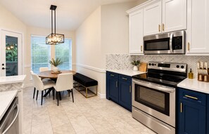A modern kitchen with white cabinets, a black stove, and a dining area with a bench.