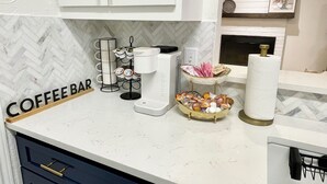 A kitchen with white cabinets, a coffee bar sign, a coffee machine, a paper towel holder, and a basket of snacks. - Remote&Travel Workers Retreat: Beautiful Rockwall home near the Harbor (Rockwall)