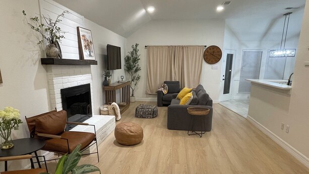 A modern living room with a fireplace, sofa, ottoman, and a dining area with a table and chairs. - Remote&Travel Workers Retreat: Beautiful Rockwall home near the Harbor (Rockwall)