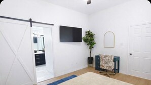 A room with a sliding door, a flat-screen TV mounted on the wall, a potted plant, a patterned cloth draped over a chair, and a blue accent rug. - Remote&Travel Workers Retreat: Beautiful Rockwall home near the Harbor (Rockwall)