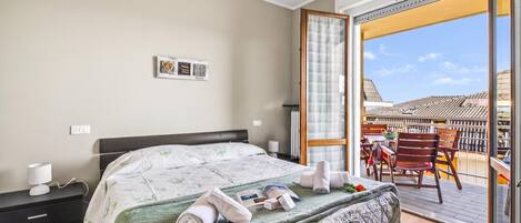 A hotel room with a bed, bedside table, lamp, and a view of the outside balcony.