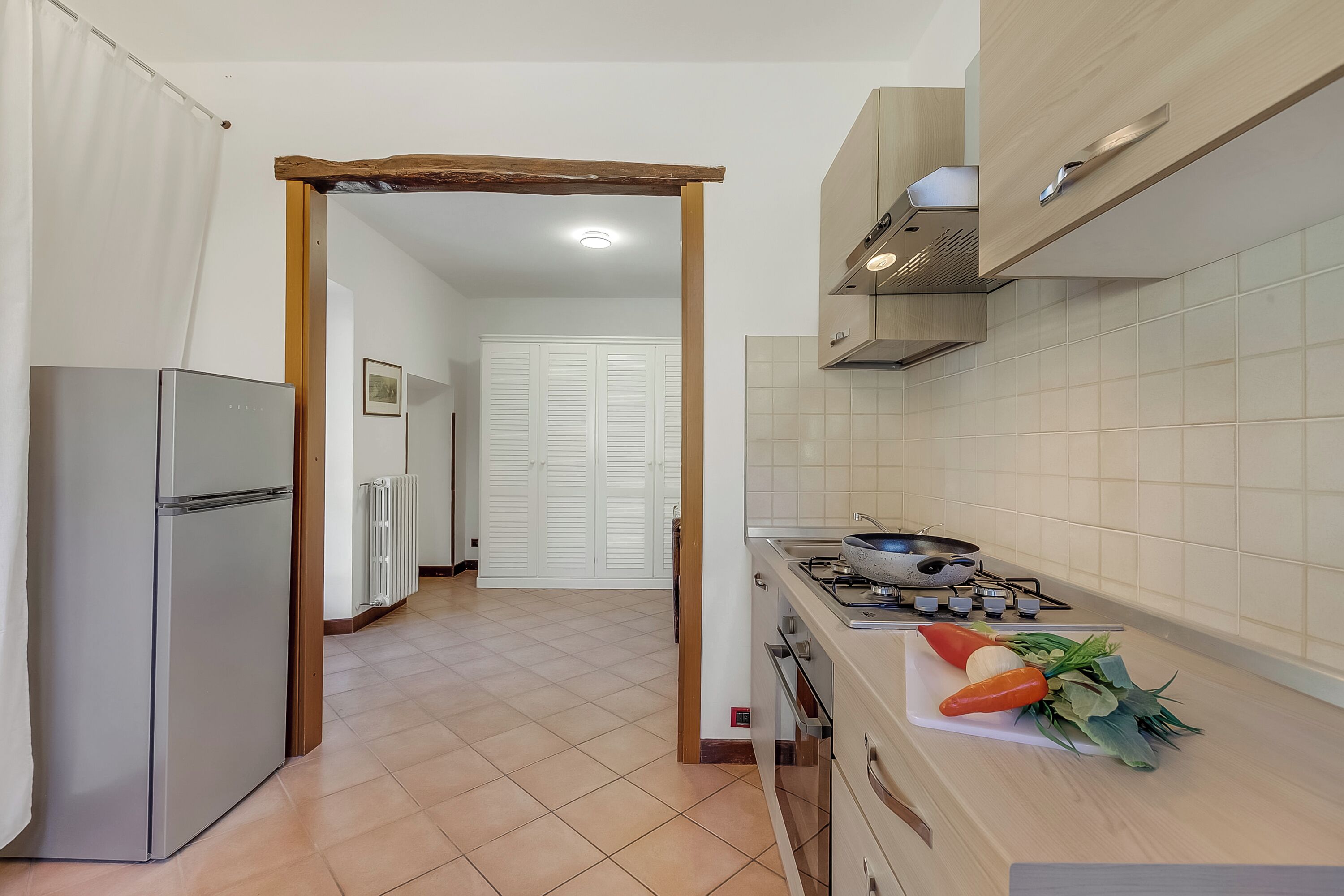 A kitchen with a refrigerator, stove, and countertop with vegetables.