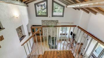 Eine Holztreppe mit einer Steinsäule und Blick auf ein Haus durch ein Fenster.