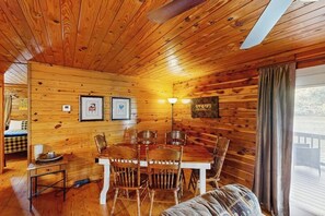 A wooden cabin interior with a dining table, chairs, a sofa, and a ceiling fan. - Delightful Riverfront Apartment w/ river access for swimming, fishing & boating (Hot Springs)