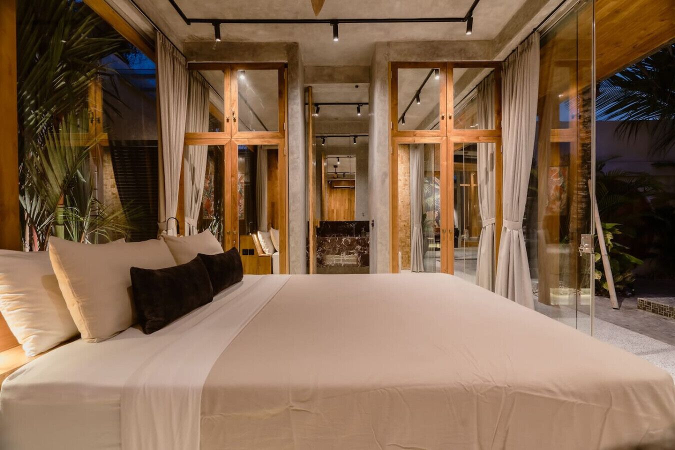 A large bed with a white bedspread and multiple pillows, a glass door leading to a balcony, and a view of the outdoors.