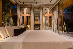 A large bed with a white bedspread and multiple pillows, a glass door leading to a balcony, and a view of the outdoors. - Best Location Honeymoon Villa Bali Canggu (Kuta Utara)