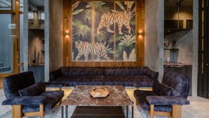 Un área de descanso moderna con un sofá, dos sillones, una mesa de centro de mármol y un gran mural en la pared que muestra un tigre entre follaje.