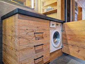 Ein kompakter, moderner Waschraum mit einer Waschmaschine von Bosch, Holzschränken und einer schwarzen Arbeitsplatte.