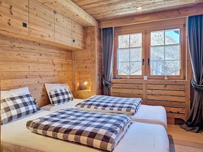 Ein Holzhütten-Zimmer mit zwei Betten, einem Fenster mit Vorhängen und einem Nachttisch mit Lampe.