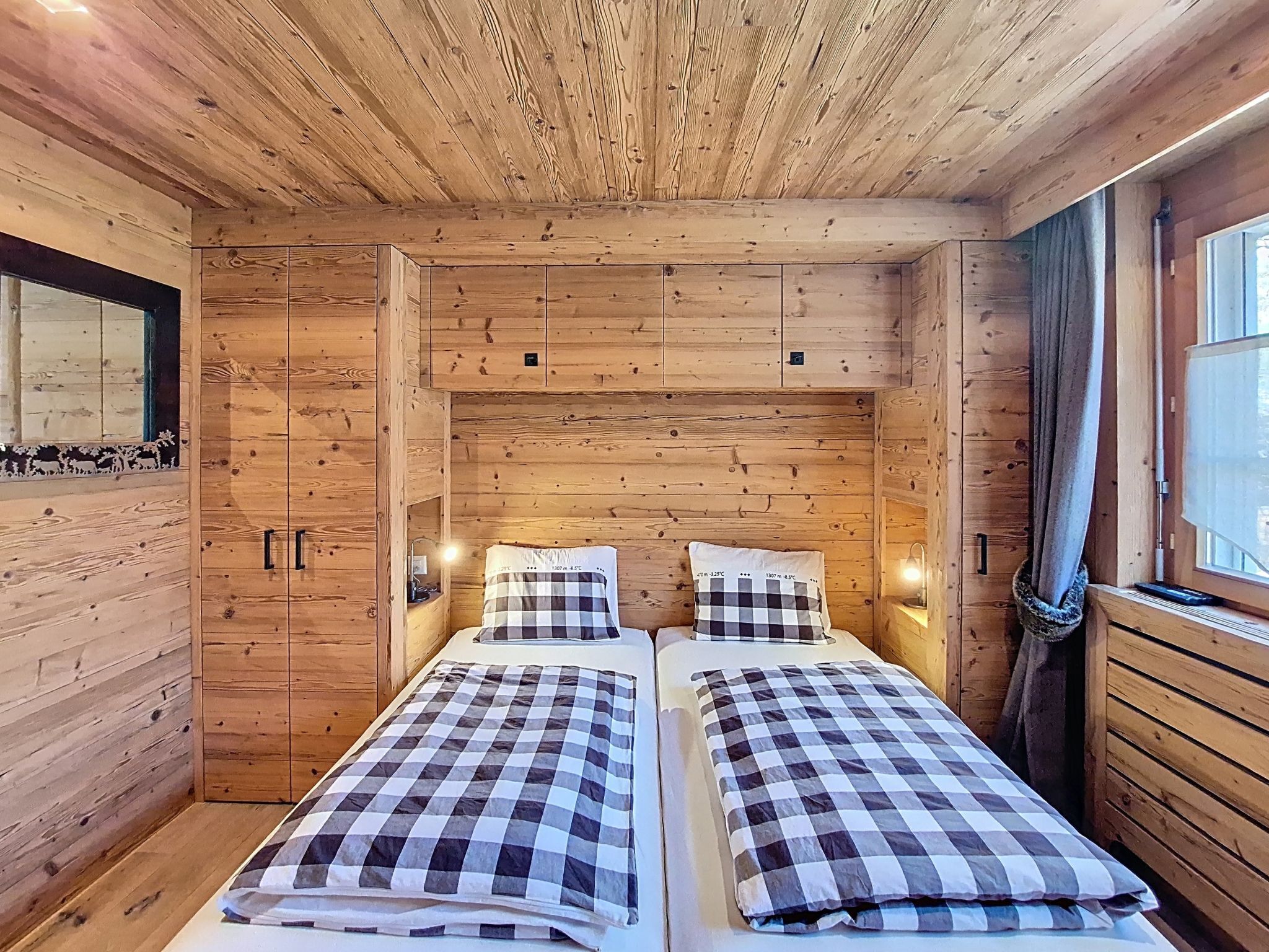 A wooden cabin room with two beds, a mirror, and a window.