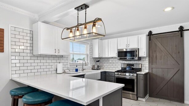 A kitchen with white cabinets, a large island with stools, a hanging light fixture, a microwave, and a stove. - Premier Louisville home with exclusive home gym! (Louisville)