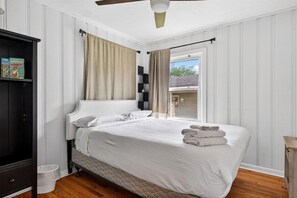 Une chambre à coucher avec un lit, une armoire, un ventilateur de plafond et une fenêtre avec des rideaux.