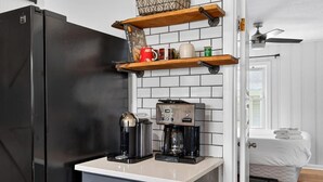 A kitchen with a black refrigerator, coffee maker, and shelves with mugs and a basket. - Premier Louisville home with exclusive home gym! (Louisville)