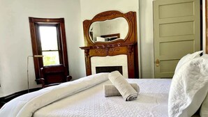 A neatly made bed with a quilted cover, a rolled towel, and a pillow. There is a wooden chair, a mirror, and a door in the room. - Exclusive 7BR Highlands home near KY Bourbon trail (Louisville)