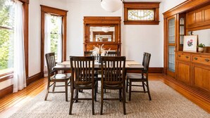 A dining room with a wooden table, chairs, a chandelier, and a large window with curtains. - Exclusive 7BR Highlands home near KY Bourbon trail (Louisville)