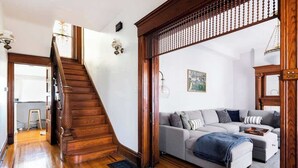 A staircase with wooden railings, a grey sofa with multiple cushions, and a wooden floor. - Exclusive 7BR Highlands home near KY Bourbon trail (Louisville)