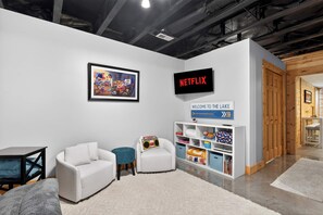 A modern living room with a white sofa, a small round table, a bookshelf, and a sign that reads 'WELCOME TO THE LAKE.' - Expansive lakefront cabin with game room and yard! (Leitchfield)
