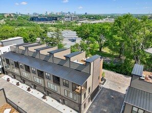 A modern multi-story building with a flat roof, large windows, and a view of a city skyline in the background. - Iconic retreat w/ exclusive rooftop lounge & spa! (Nashville)