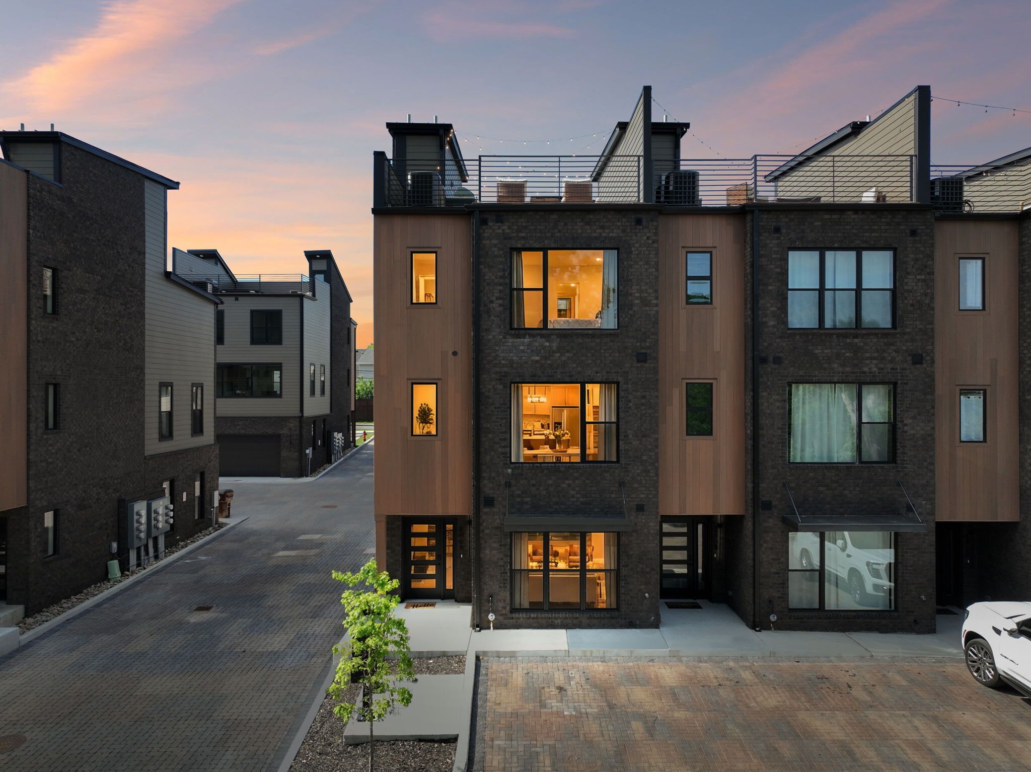 A modern multi-story residential building with visible balconies, large windows, and a driveway.
