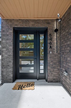 A black-framed door with a glass panel, a brick wall, a number '546A' sign, and a 'Hello' mat. - Iconic retreat w/ exclusive rooftop lounge & spa! (Nashville)