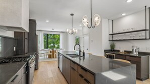 A modern kitchen with a central island, stainless steel appliances, and a dining area with a view. - Iconic retreat w/ exclusive rooftop lounge & spa! (Nashville)