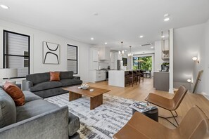A modern living room with a grey sofa, a coffee table, and a brown leather chair. - Exclusive townhome ft. rooftop lounge w/ hot tub! (Nashville)