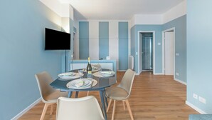 A modern dining area with a round table, chairs, a flat-screen TV, and a kitchen in the background. - Kenyon Charm - Total Sea View, Alassio, Italy (Alassio)