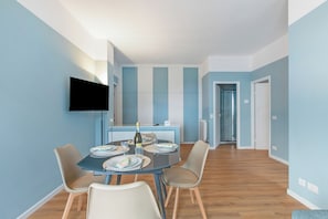 A modern dining area with a round table, chairs, a flat-screen TV, and a kitchen in the background. - Kenyon Charm - Total Sea View, Alassio, Italy (Alassio)