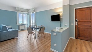 A modern living room with a sofa, dining table, chairs, a TV, and a wooden door. - Kenyon Charm - Total Sea View, Alassio, Italy (Alassio)