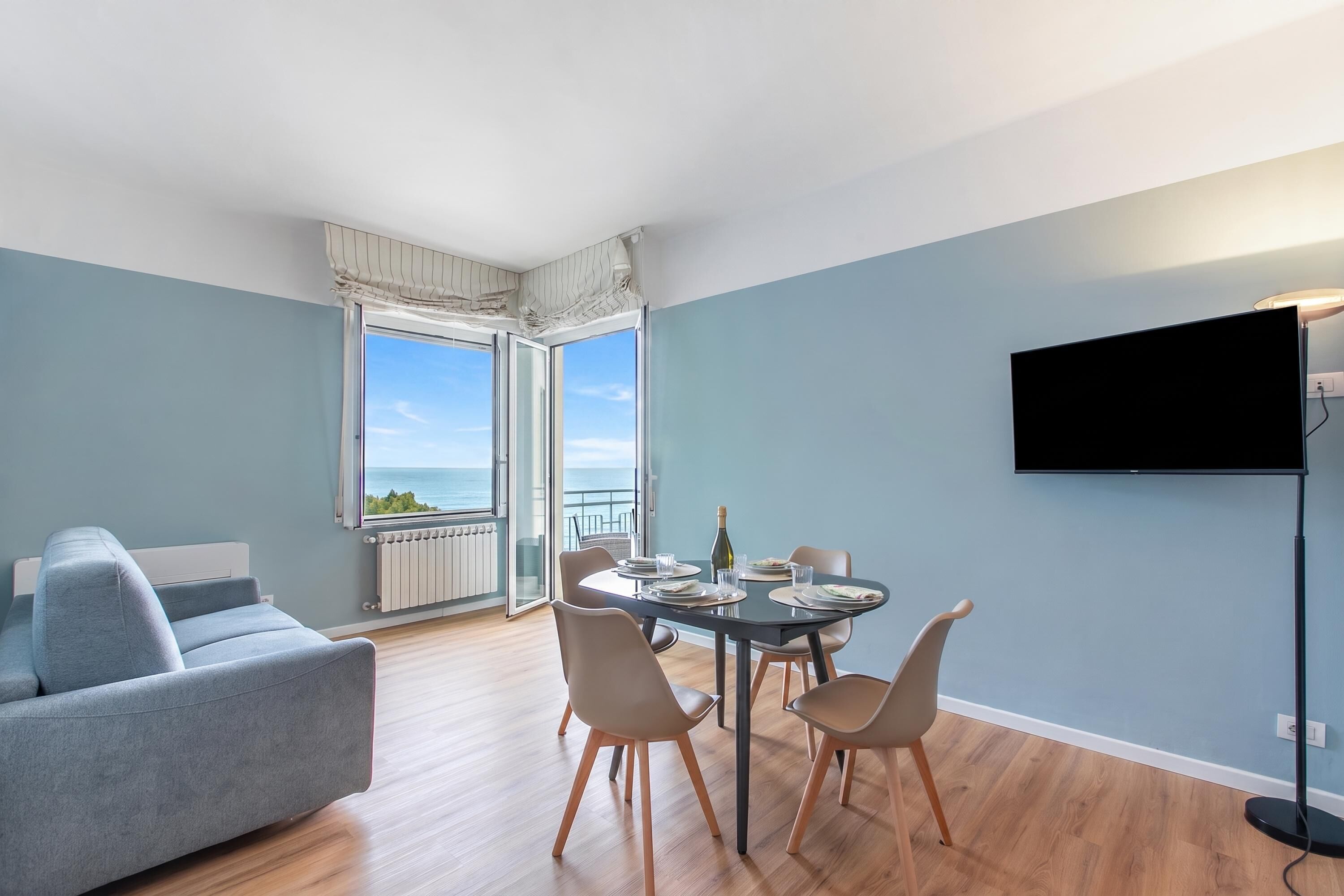 Ein modernes Wohnzimmer mit einer Couch, einem Esstisch, Stühlen, einem Fernseher und Meerblick.