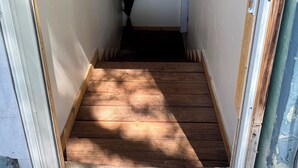 Un pasillo estrecho con suelo de madera, un jarrón con plantas secas y un marco de puerta a la derecha.