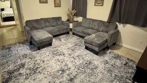 Una sala de estar con un sofá modular, una alfombra estampada, una lámpara de techo y una pared con cuadros y un letrero.