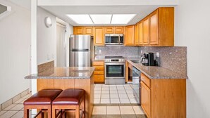 Una cocina compacta con armarios de madera, un refrigerador de acero inoxidable, un microondas, un horno y una cafetera.
