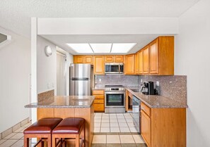 Eine kompakte Küche mit Holzausbau, einem Edelstahlkühlschrank, einer Mikrowelle, einem Backofen und einer Kaffeemaschine.