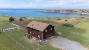Een tweelaags houten huis met een omheinde tuin, een garage en uitzicht op de oceaan.