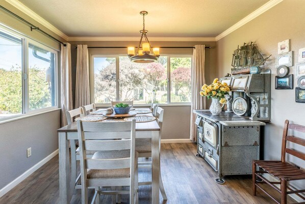 A dining area with a table set for four, a chandelier, and a view of the outdoors through large windows. - Say goodbye to worries and hello to a dream beach vacation at Dust-off Sand! (Fort Bragg)