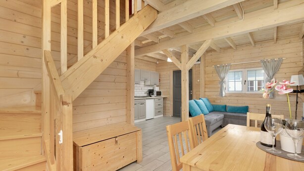 Un interior de madera con una escalera, una mesa de comedor con sillas, un sofá y una zona de cocina.