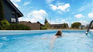 Piscina residencial con una persona nadando, rodeada de casas y un cielo despejado.