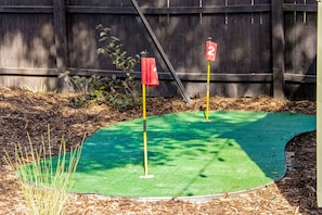 A miniature golf course with two numbered holes, surrounded by a wooden fence and mulch. - Bright Beautiful 2BR Near Broadmoor with King Bed, Hot Tub, Deck & Putting Green (Colorado Springs)